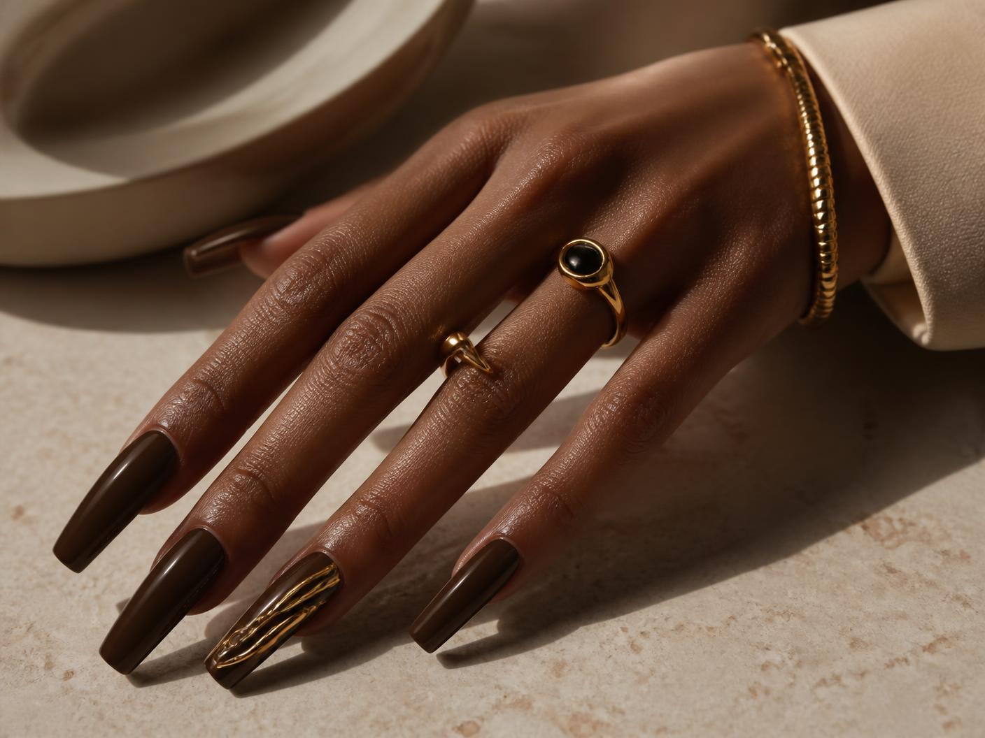 Long coffin nails in deep espresso with a restrained sculptural gold accent nail, styled with gold jewellery